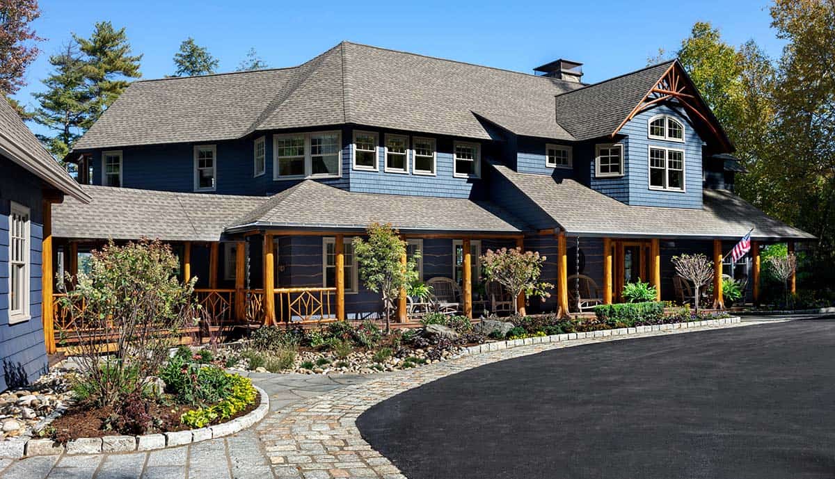 Adirondack-style lake house exterior with blue shingle siding, cedar log porch columns, and circular driveway