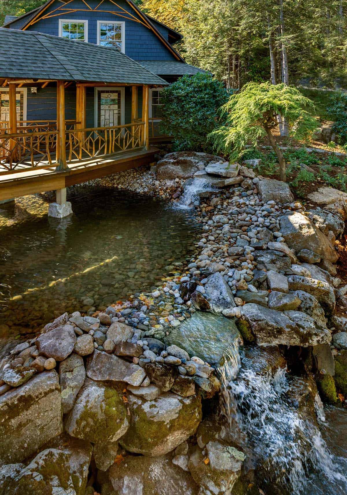 Rustic house with cedar porch overhanging a natural rock waterfall and pond