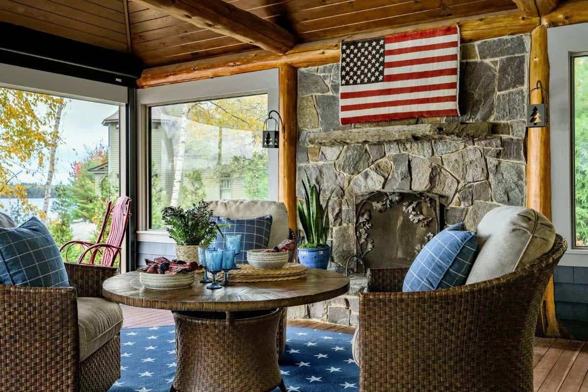 Screened porch with stone fireplace, wicker furniture, American flag wall art, and lake views
