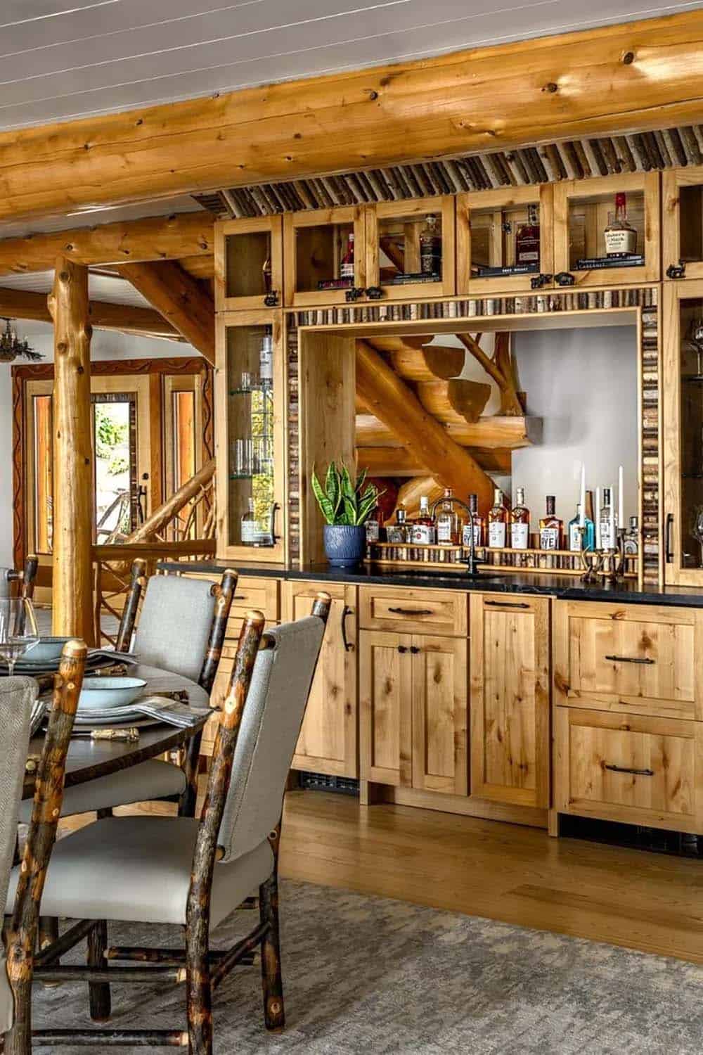 Rustic bar area with knotty pine cabinetry, birch trim, log beam ceiling, and whiskey bottle display