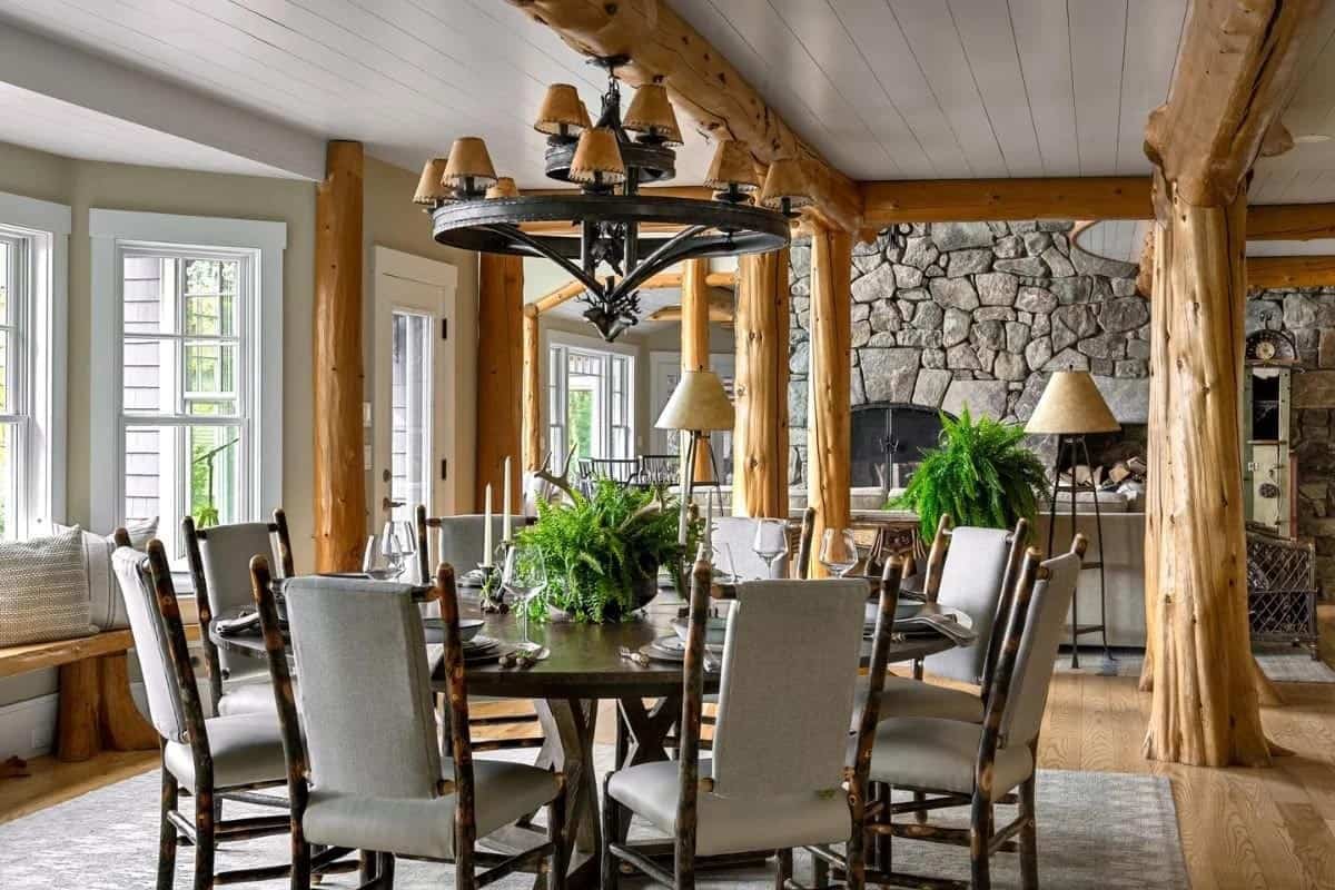 Dining room with log beam columns, round table, hickory chairs, antler chandelier, and stone fireplace
