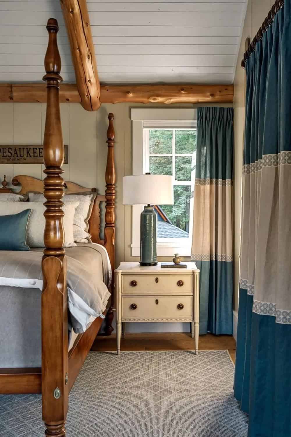 Guest bedroom with four-poster wood bed, teal velvet drapes, log ceiling beam, and antique nightstand