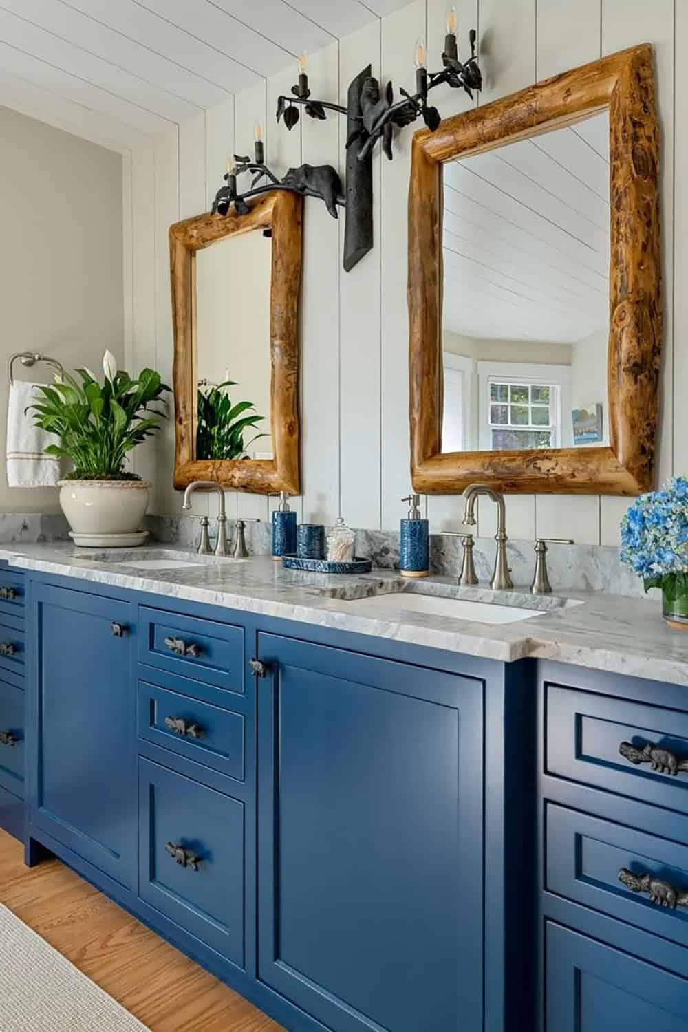 Primary bathroom double vanity with navy blue cabinets, marble countertops, and rustic log-framed mirrors