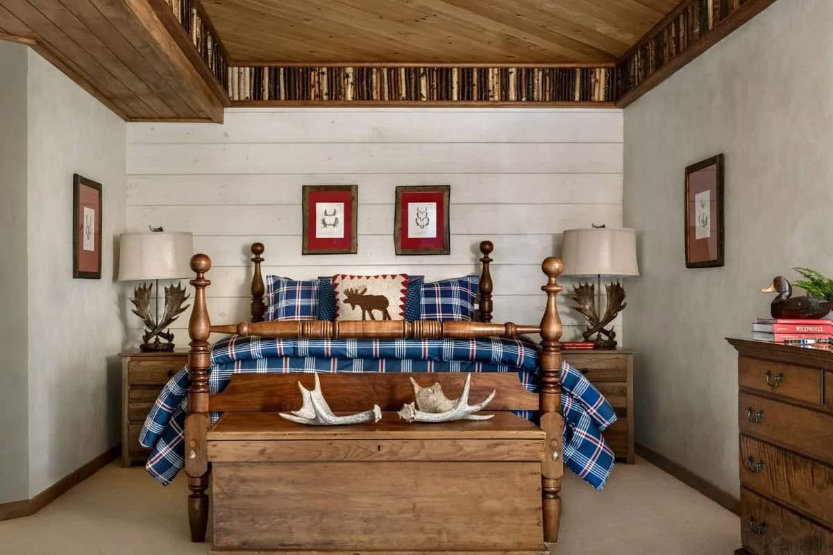 Cabin-style bedroom with plaid bedding, four-poster bed, antler décor, and birch log ceiling trim