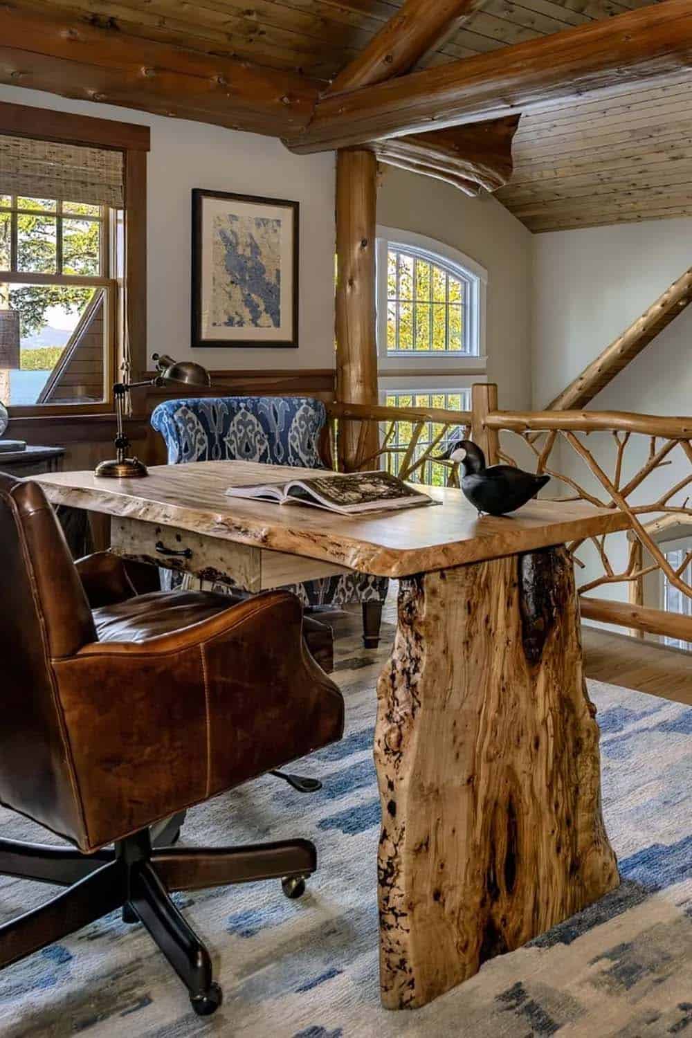Home office loft with live-edge wood desk, leather chair, branch railing, and lake views