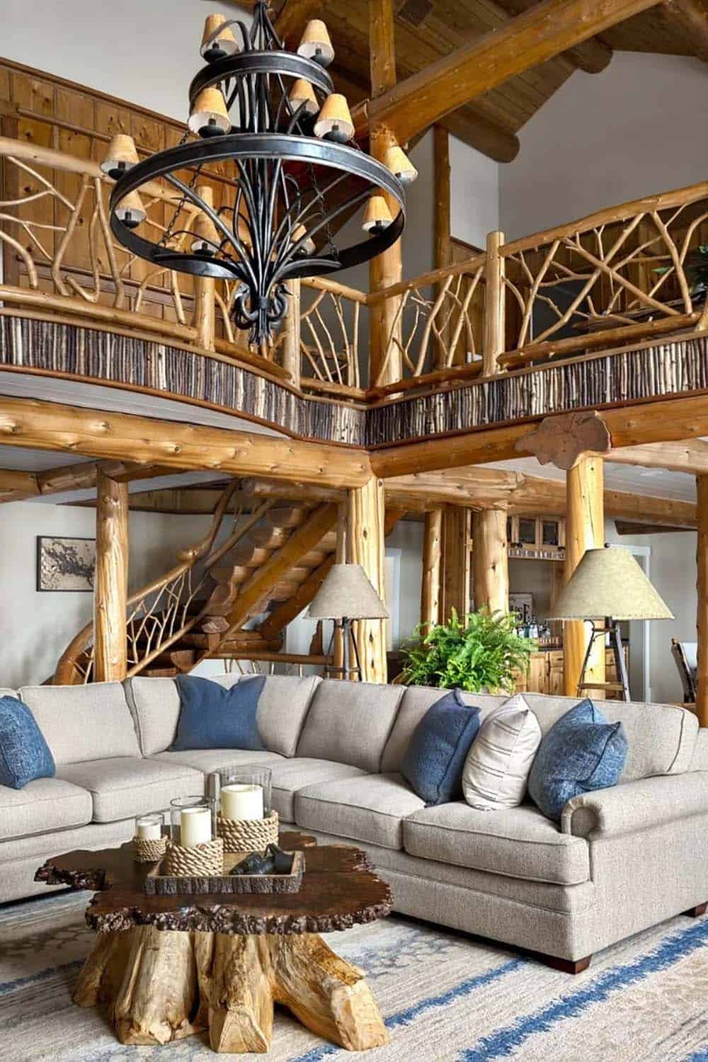 Great room interior with double-height log beam ceiling, twig balcony railing, and large sectional sofa