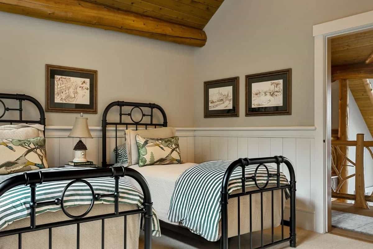 Twin bedroom with black iron beds, green striped bedding, wainscoting, and log ceiling beam