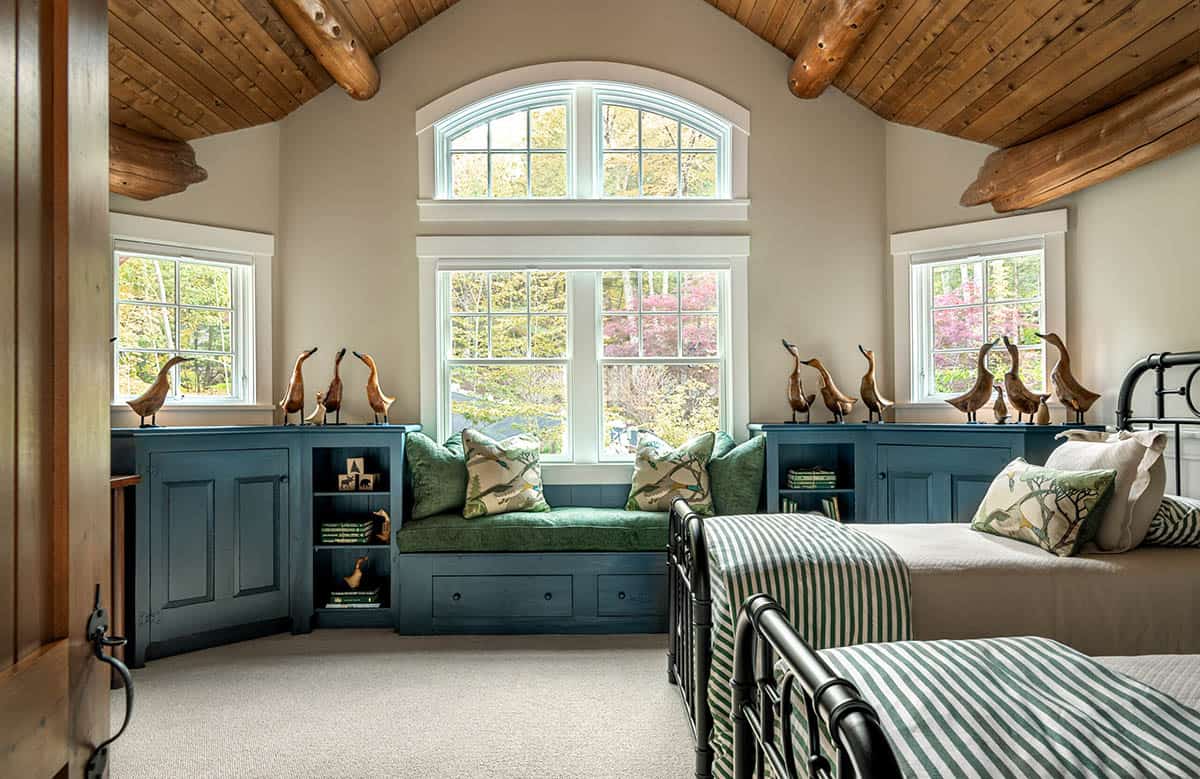 Twin bedroom with vaulted log ceiling, teal built-in storage bench, arched window, and wooden duck figurines