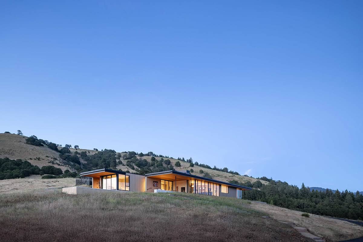 Modern wood-clad home glowing at dusk against a forested hillside