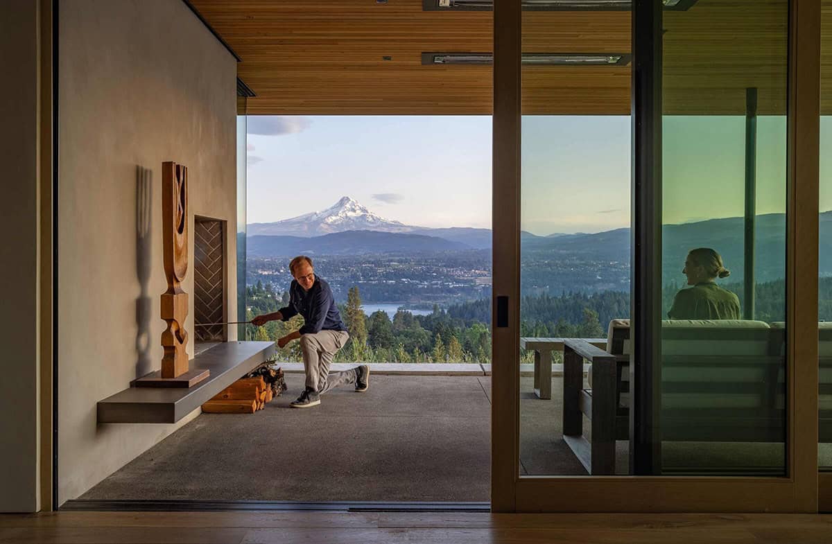 Man lighting a fireplace on an outdoor terrace with a panoramic mountain and river view