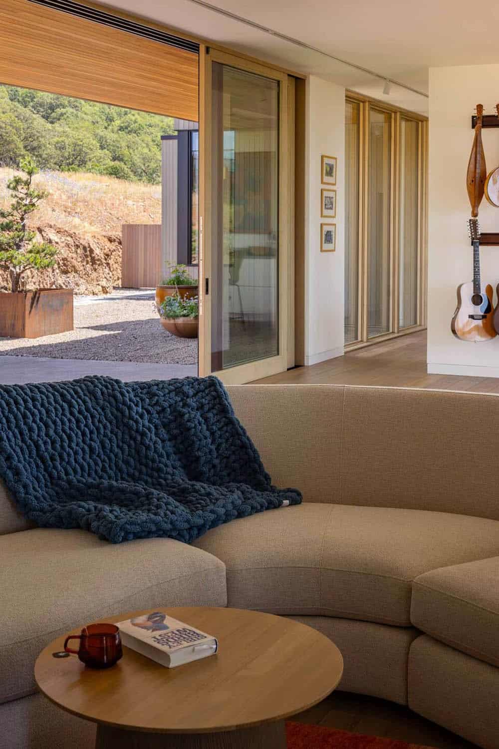 Curved sectional sofa with chunky knit throw facing open sliding doors to a courtyard