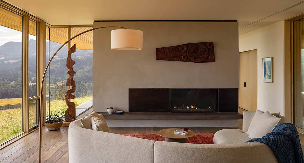 Living room with curved sofa, linear gas fireplace, wood sculpture, and floor-to-ceiling mountain views