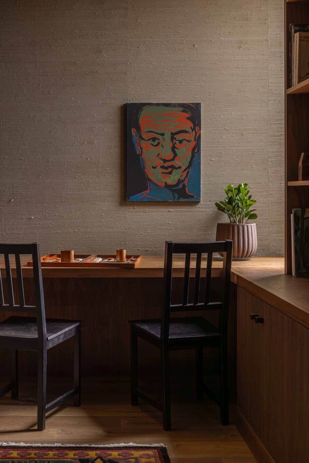 Dark reading nook with walnut desk, built-in shelving, and a bold portrait painting