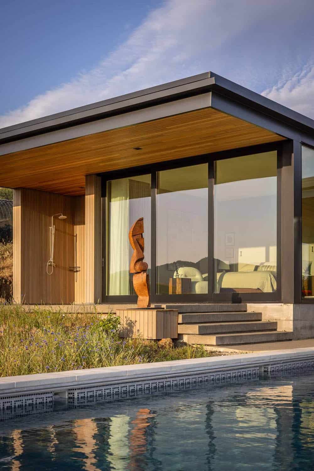 Pool pavilion with floor-to-ceiling glass, wood ceiling, outdoor shower, and abstract wood sculpture