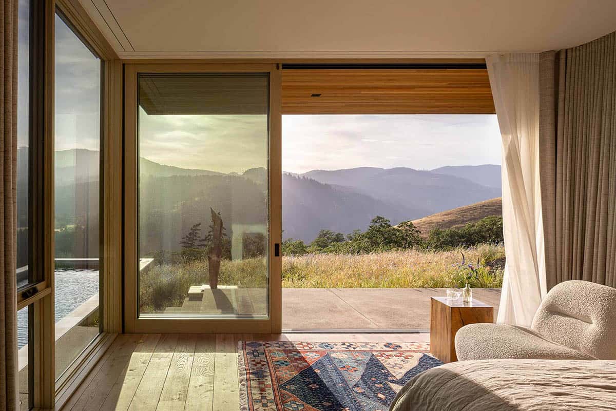 Primary bedroom with sliding glass doors open to a terrace overlooking rolling hills at sunset