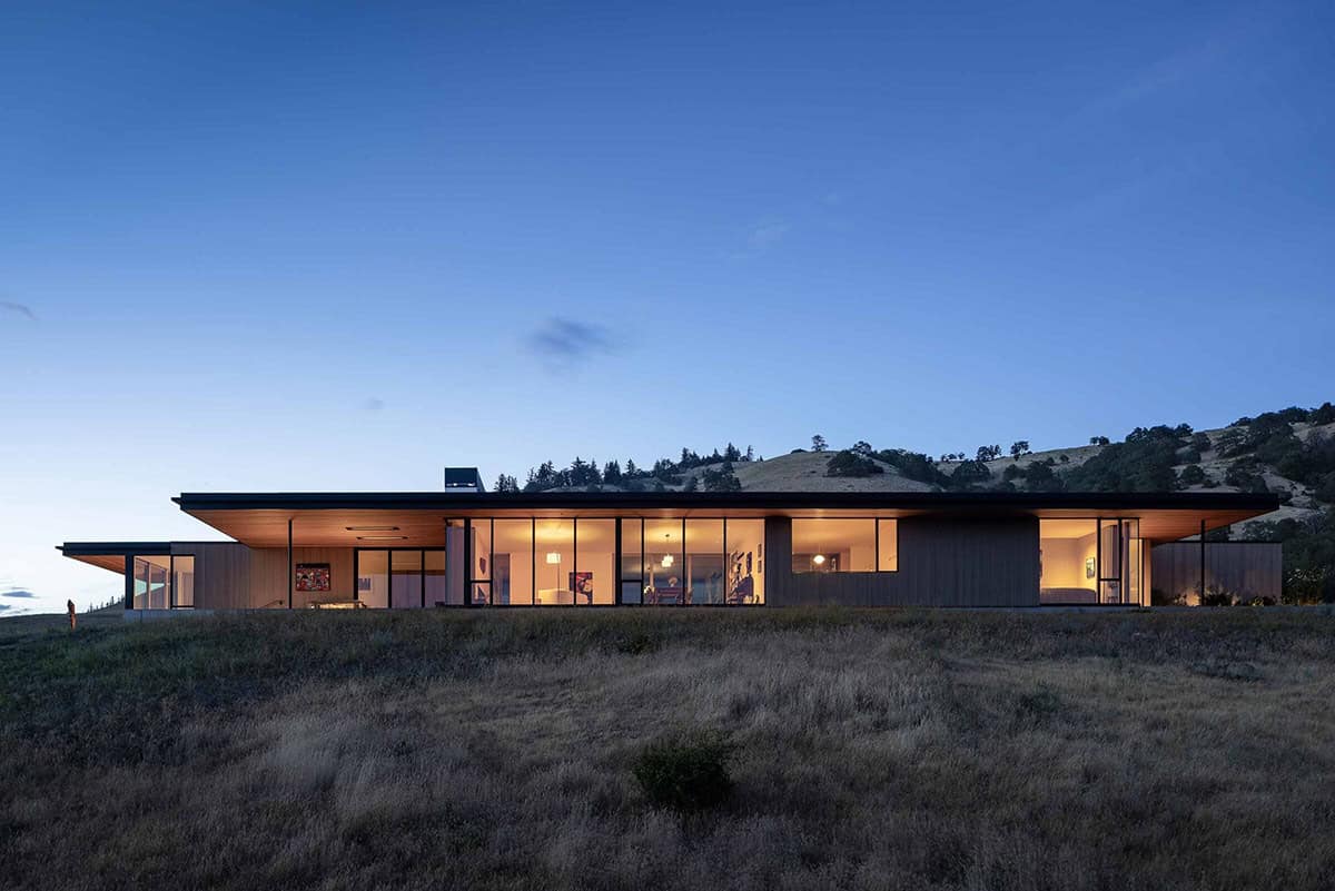 Modern single-story home glowing warmly at dusk with floor-to-ceiling glazing across its full length