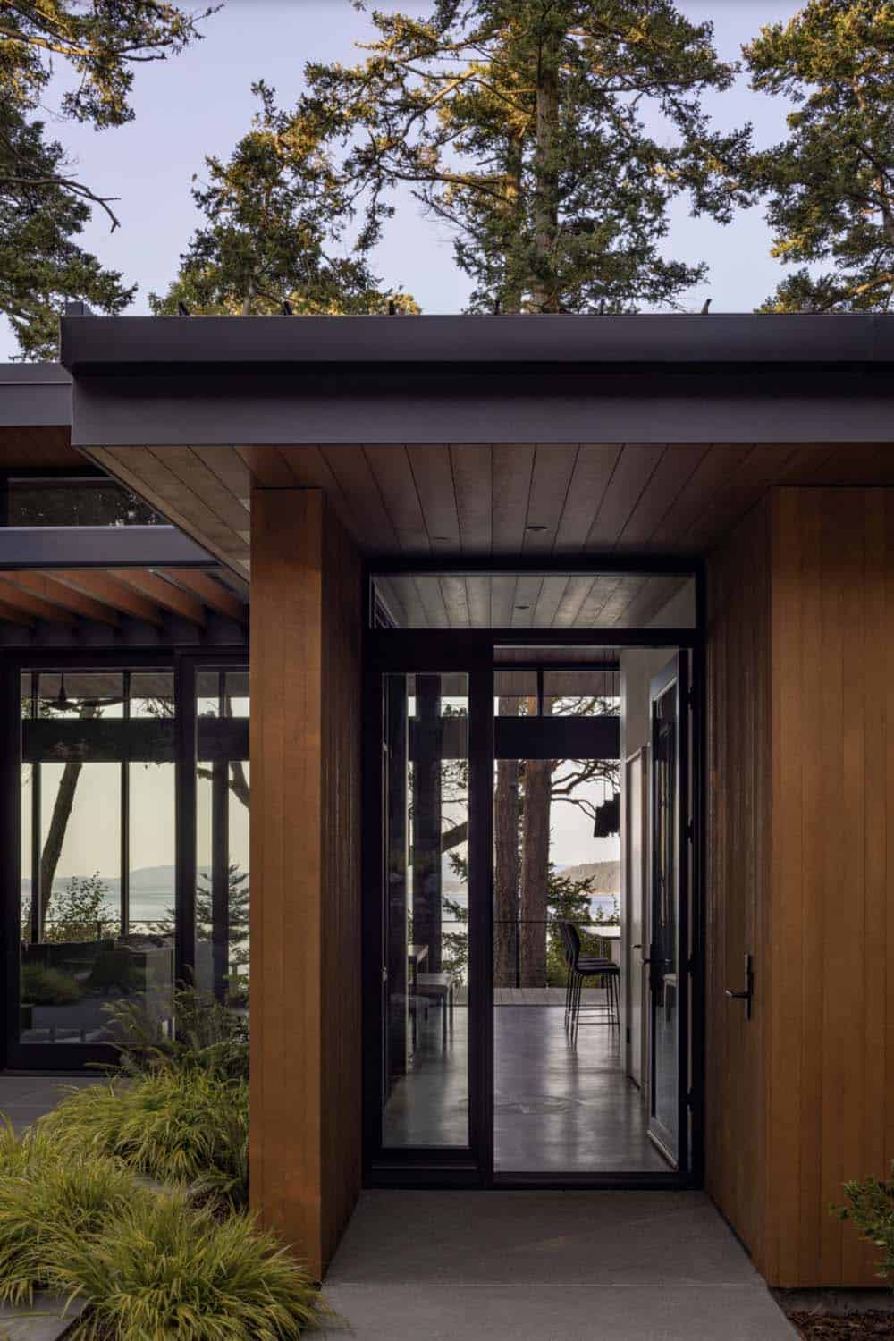 Close-up of black-framed glass entry door with cedar surround and water views beyond
