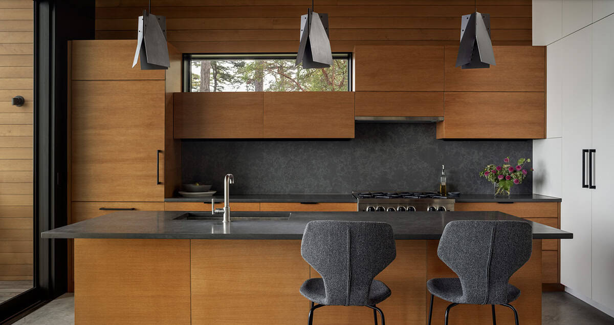 Modern kitchen with flat-front cedar cabinetry, dark stone countertops and backsplash, and angular black pendant lights