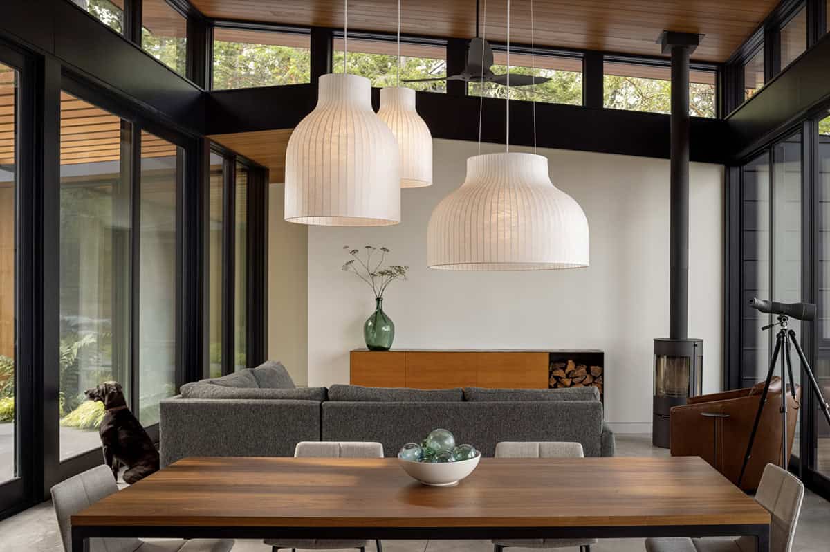 Living and dining space with large white pendant lights, gray sectional sofa, freestanding wood stove, and clerestory windows