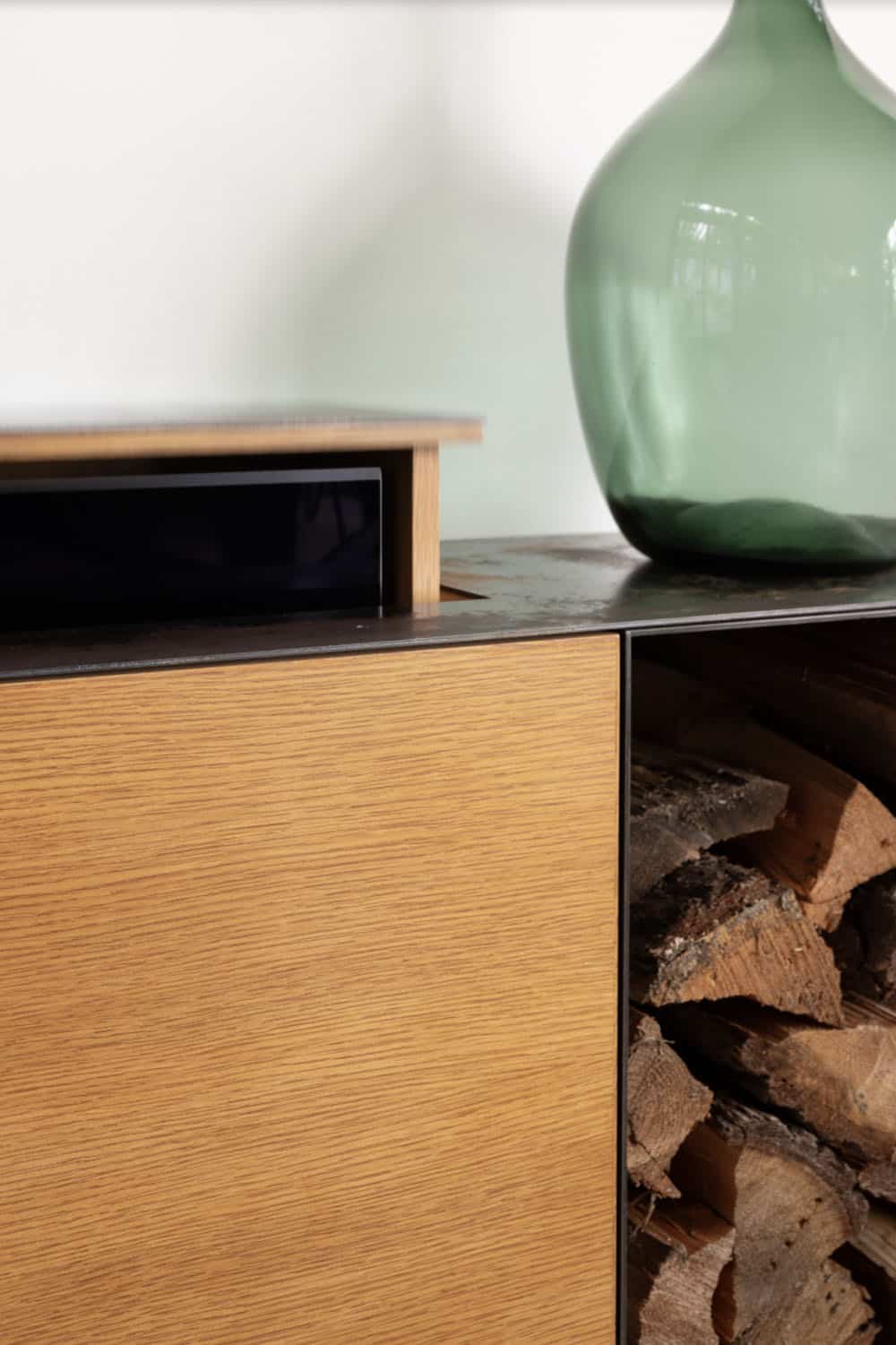 Detail of oak sideboard with hidden pull-out drawer, dark steel surface, and green glass vessel
