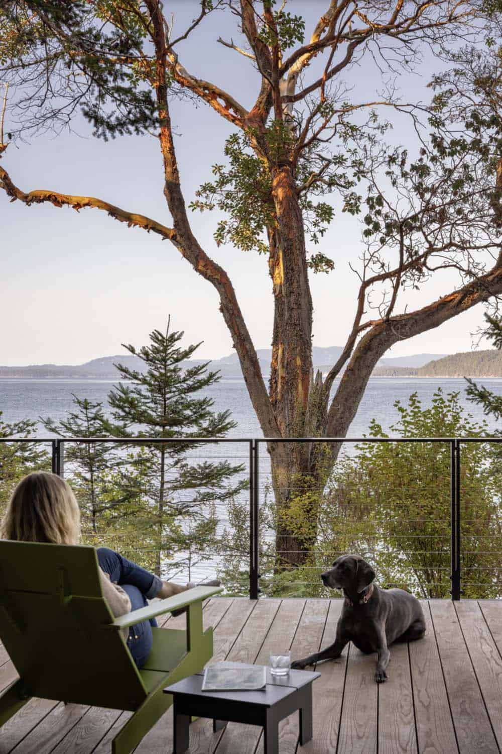 Woman and dog relaxing on waterfront deck with Adirondack chair overlooking island-dotted Puget Sound