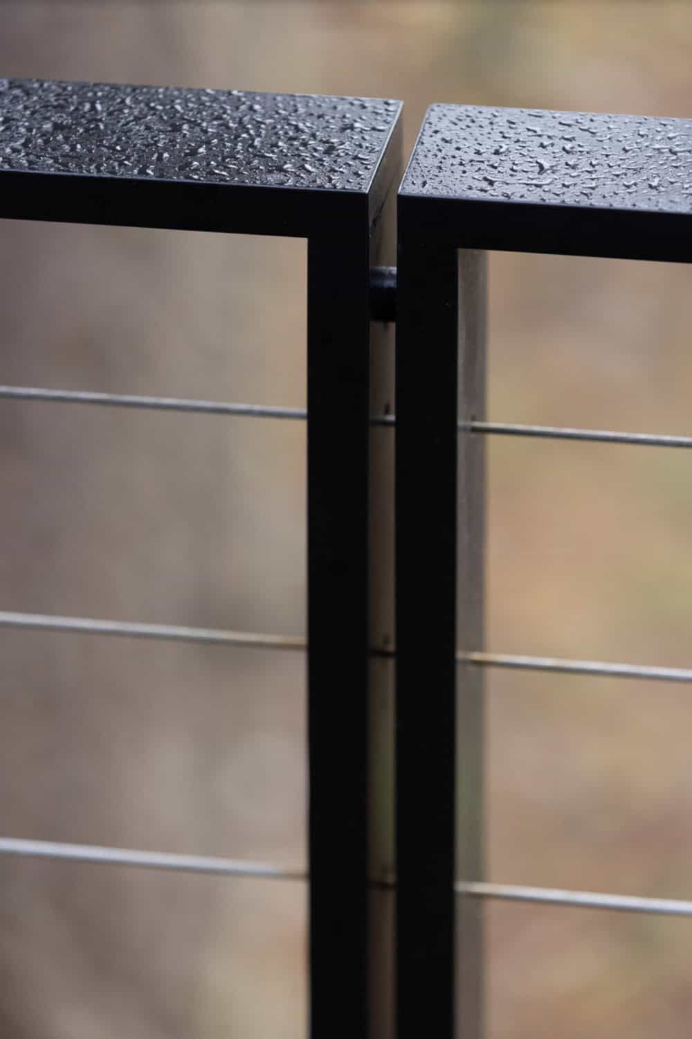 Close-up detail of wet black steel cable railing post with rain droplets