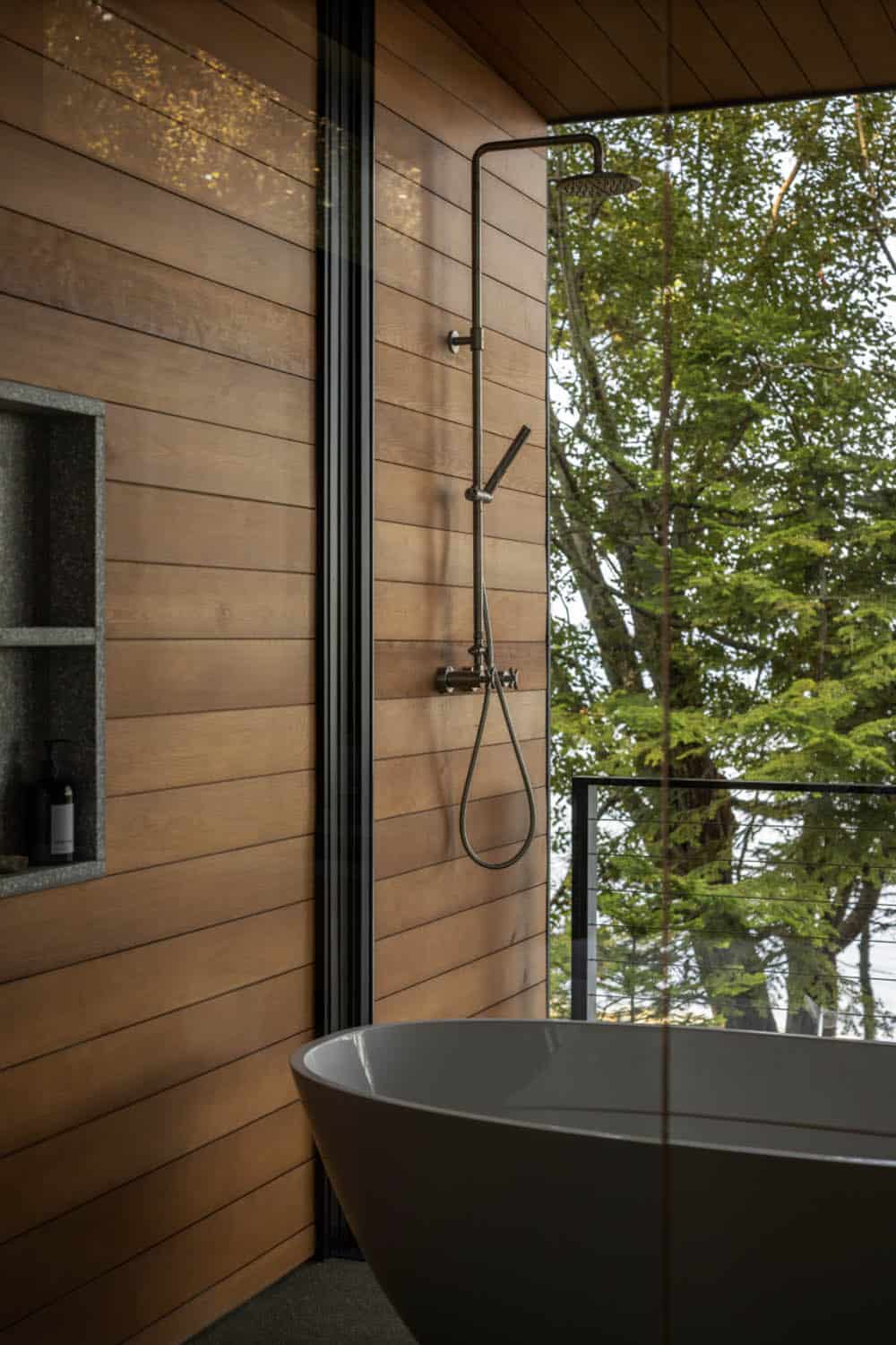 Bathroom detail with wood-clad rain shower, niche shelving, and frameless glass wall overlooking treetops
