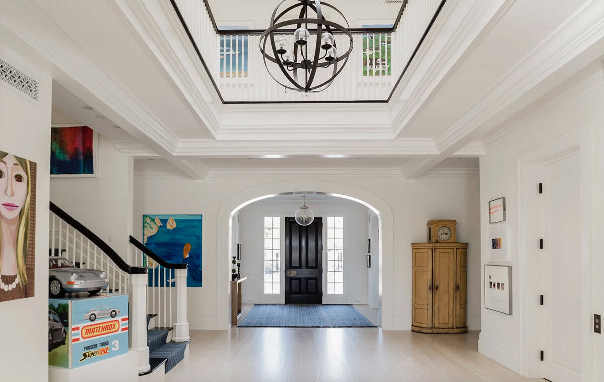 Grand white foyer with coffered ceiling, orb chandelier, arched doorway, and eclectic artwork