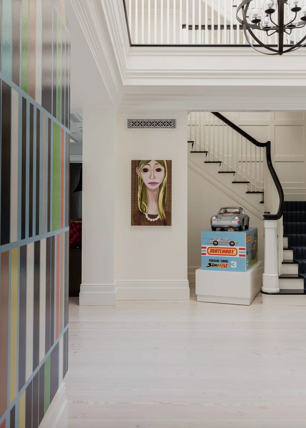 Hallway with oversized Matchbox car sculpture on white pedestal near curved staircase