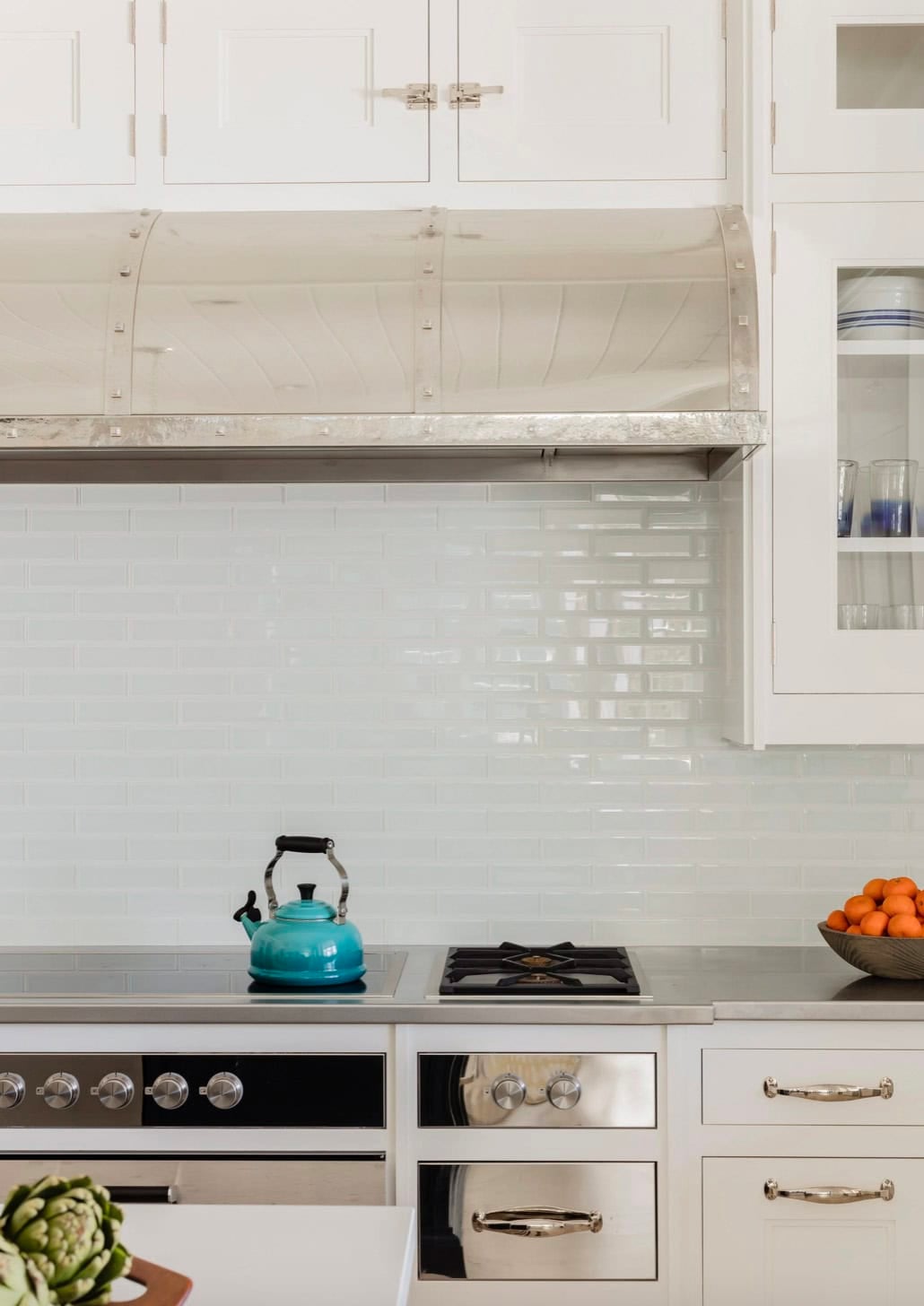 Close-up of stainless range hood, light blue subway tile backsplash, and teal kettle