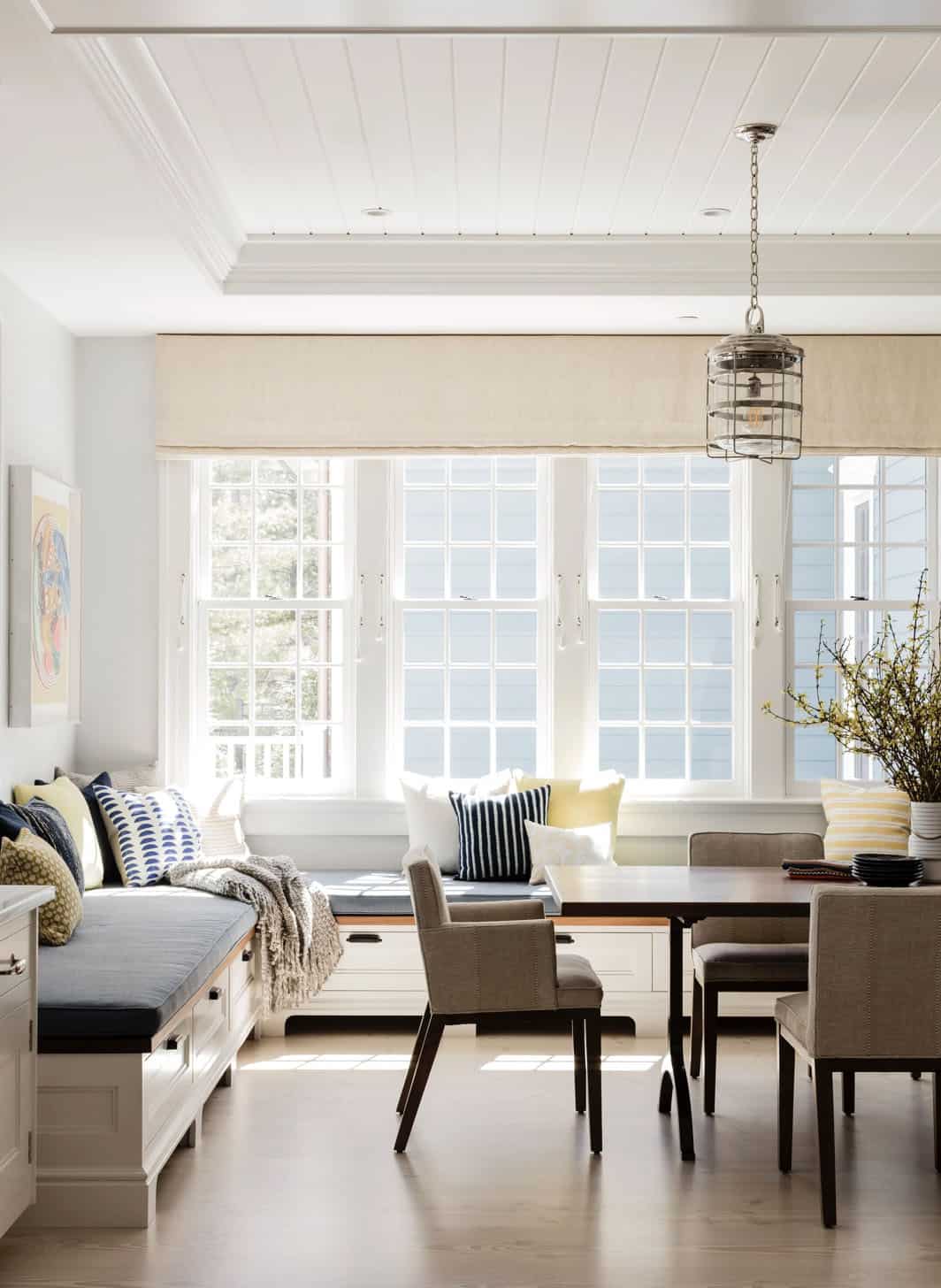 Bright breakfast nook with built-in window seat, blue cushions, and industrial pendant light