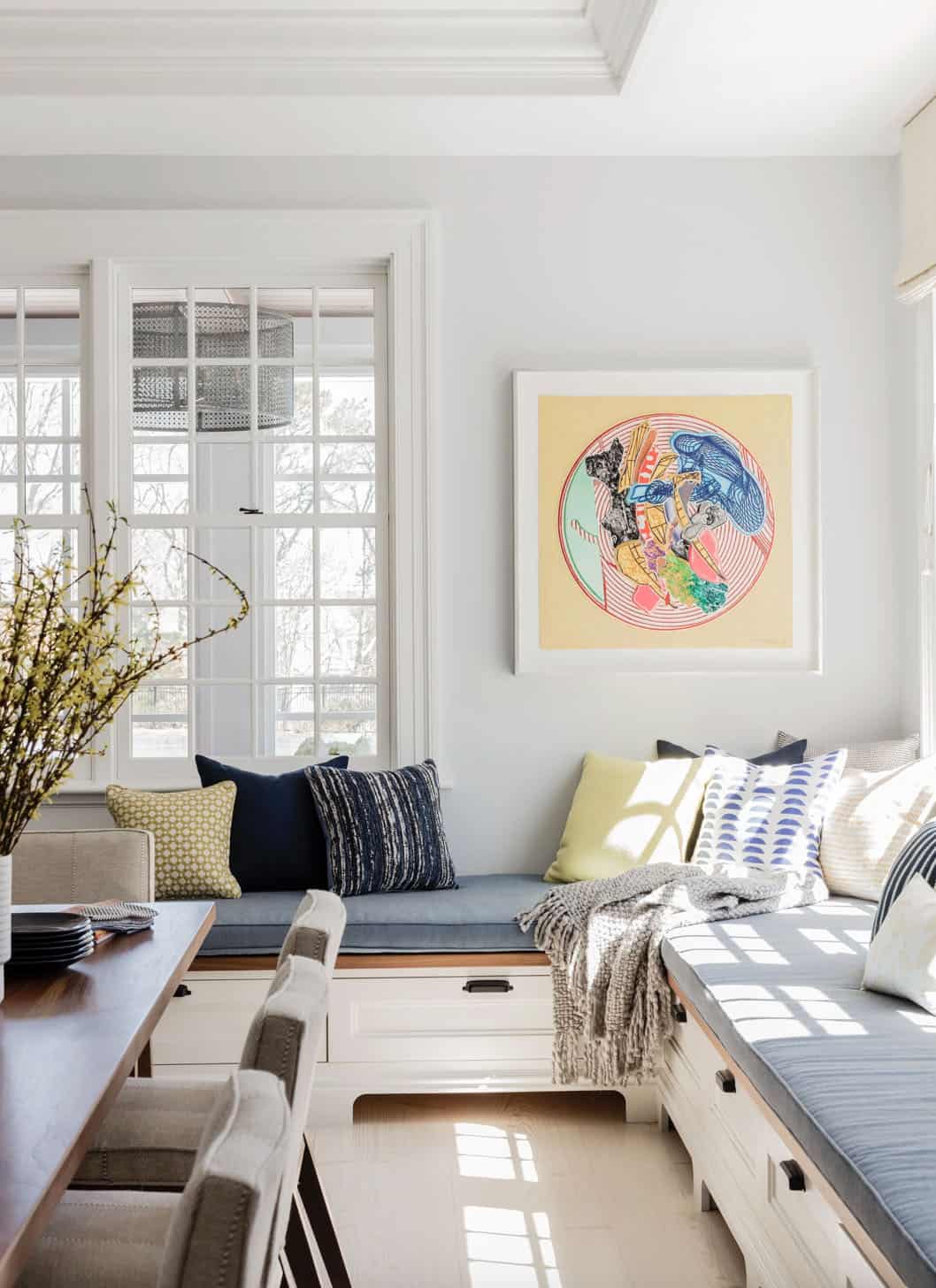 Window banquette with layered throw pillows and colorful circular artwork above
