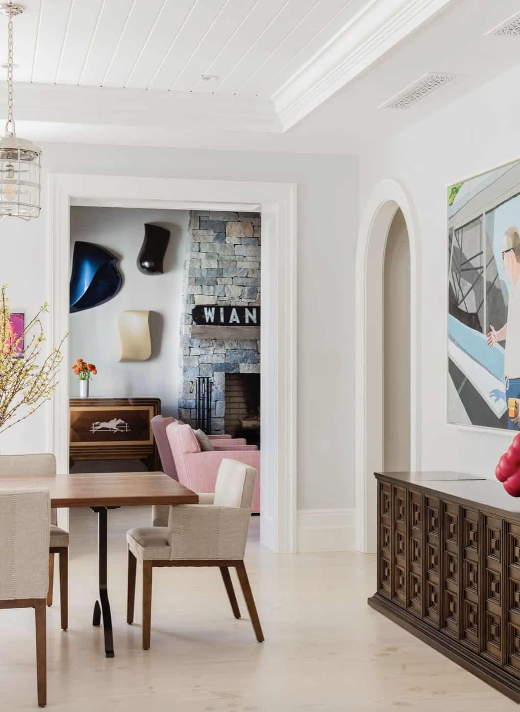 Dining area with view into living room featuring stone fireplace and pink armchairs