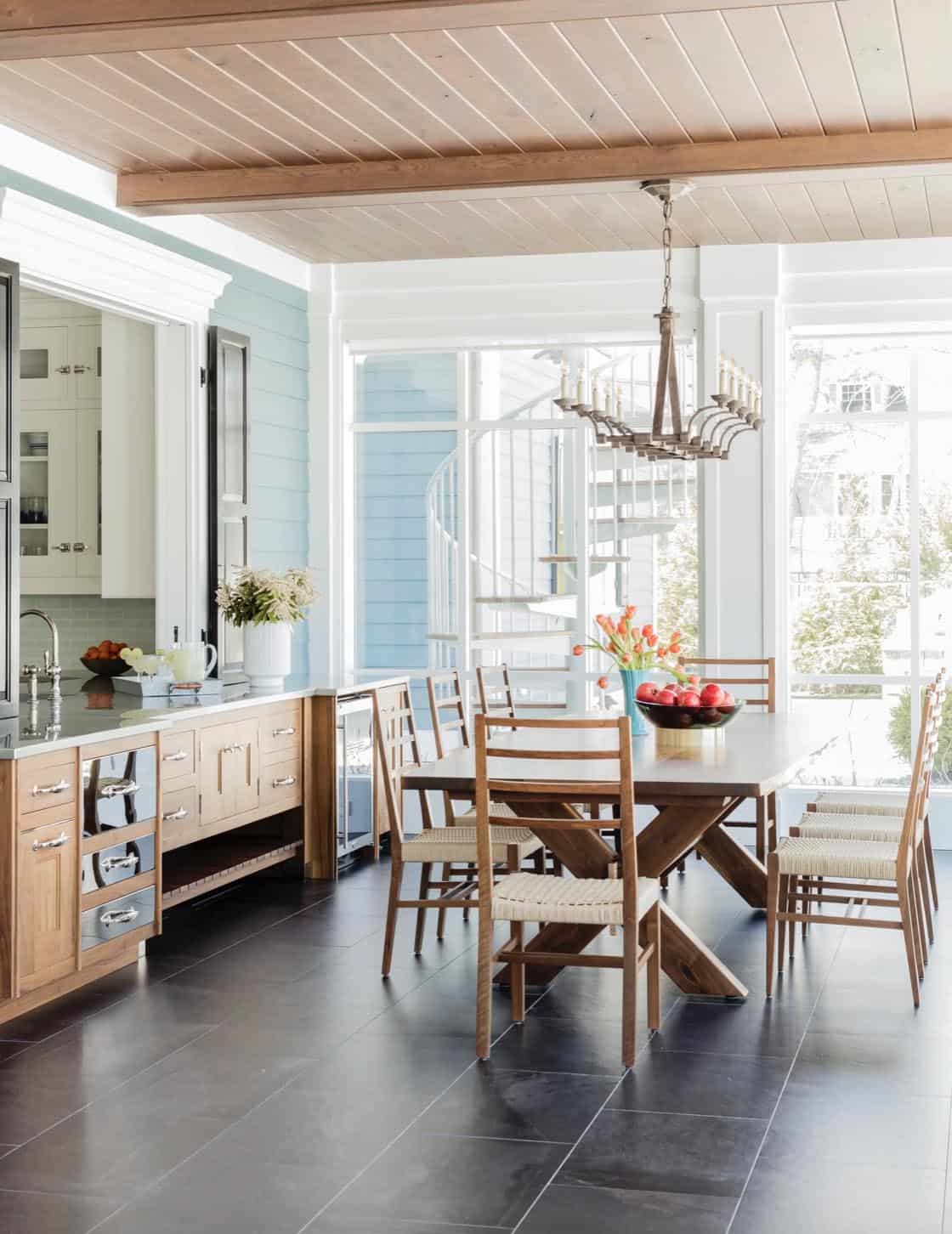 Screened porch dining area with natural wood table, ladder-back chairs, and blue shiplap walls