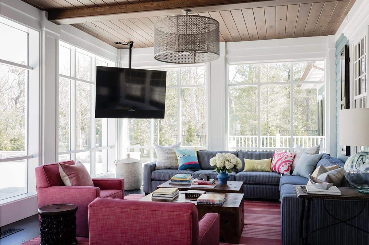 Sunroom with blue sectional, pink lounge chairs, ceiling-mounted TV, and floor-to-ceiling windows
