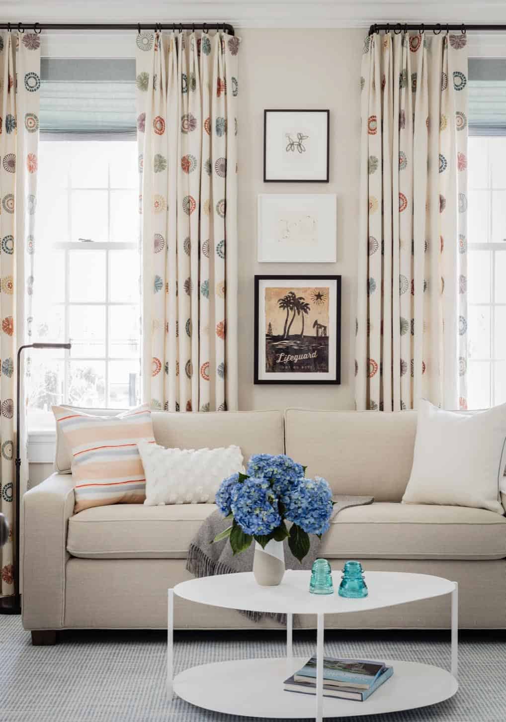 Cozy sitting room with patterned drapes, linen sofa, and stacked artwork above coffee table