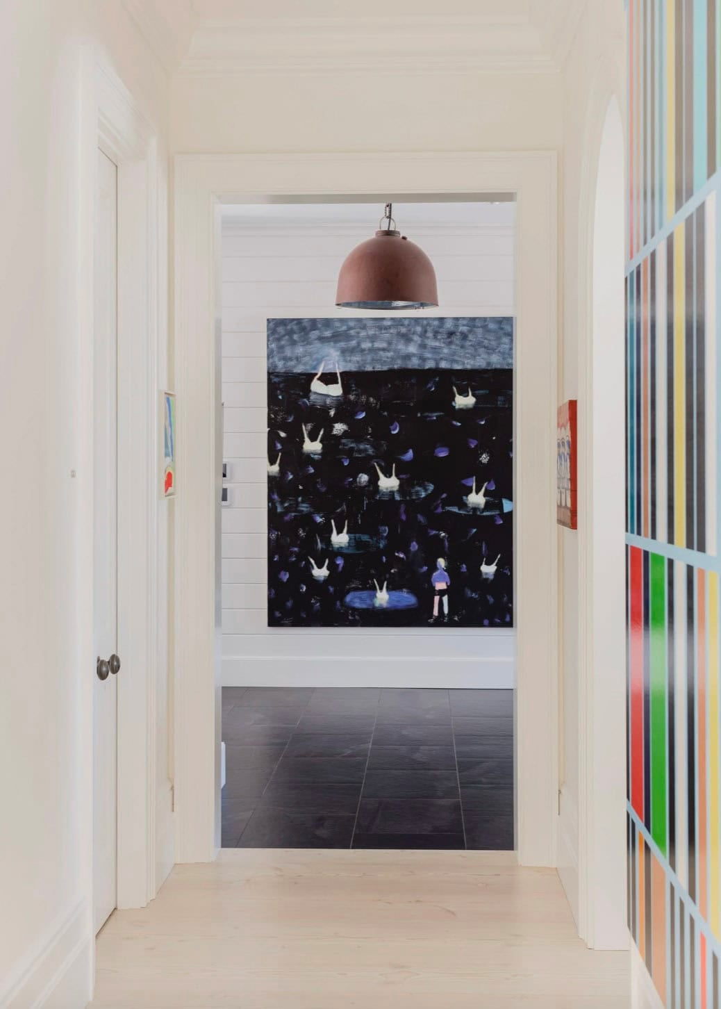 Hallway corridor with large dark swimming painting and colorful striped artwork on right wall