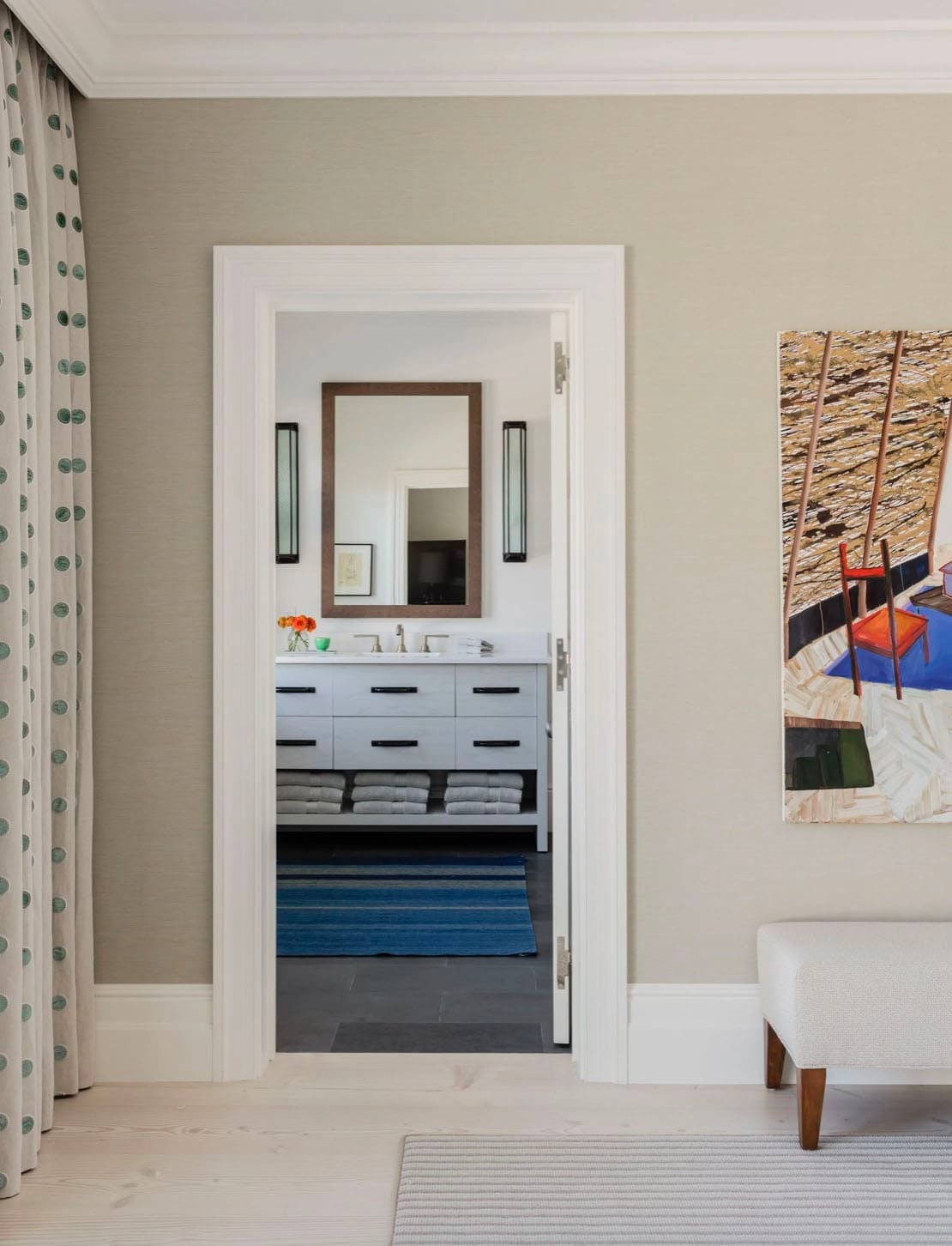 Guest bedroom doorway view into en suite bathroom with gray vanity and blue striped rug