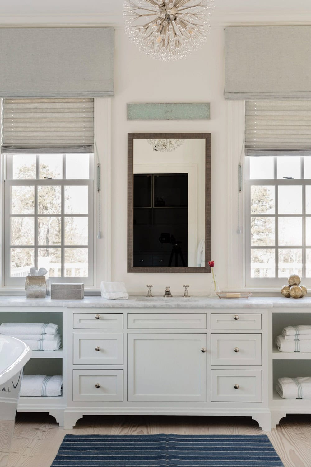 Primary bathroom with white built-in vanity, marble countertop, sputnik chandelier, and blue striped bath mat