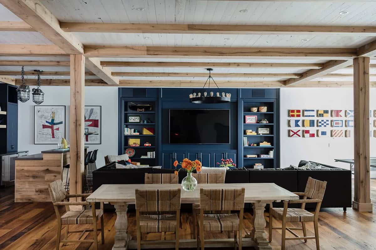 Lower level game room with navy built-in entertainment wall, rustic trestle dining table, and nautical signal flags