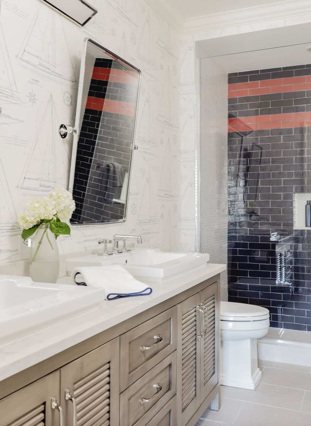 Boys' bathroom with sailboat blueprint wallpaper, gray louvered vanity, and dark subway tile shower with red accent stripe