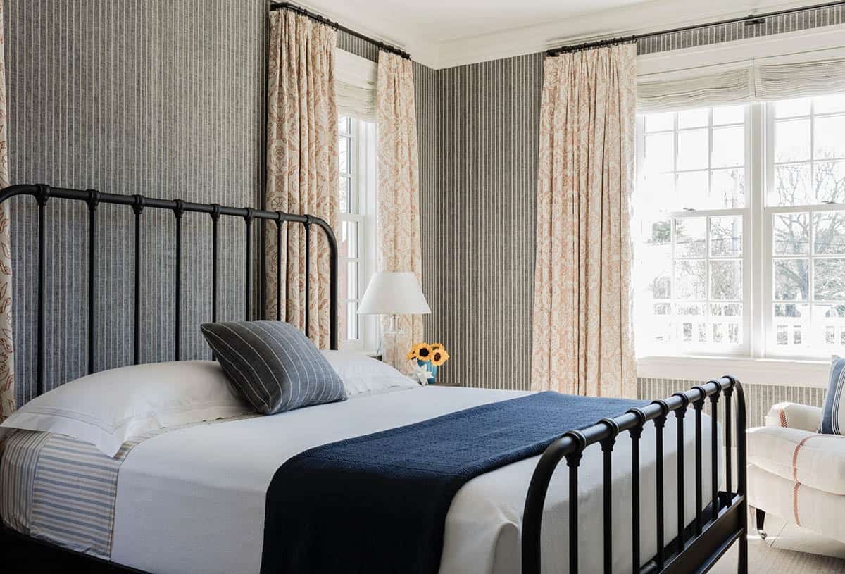 Guest bedroom with gray striped wallpaper, black iron bed frame, floral drapes, and navy quilt