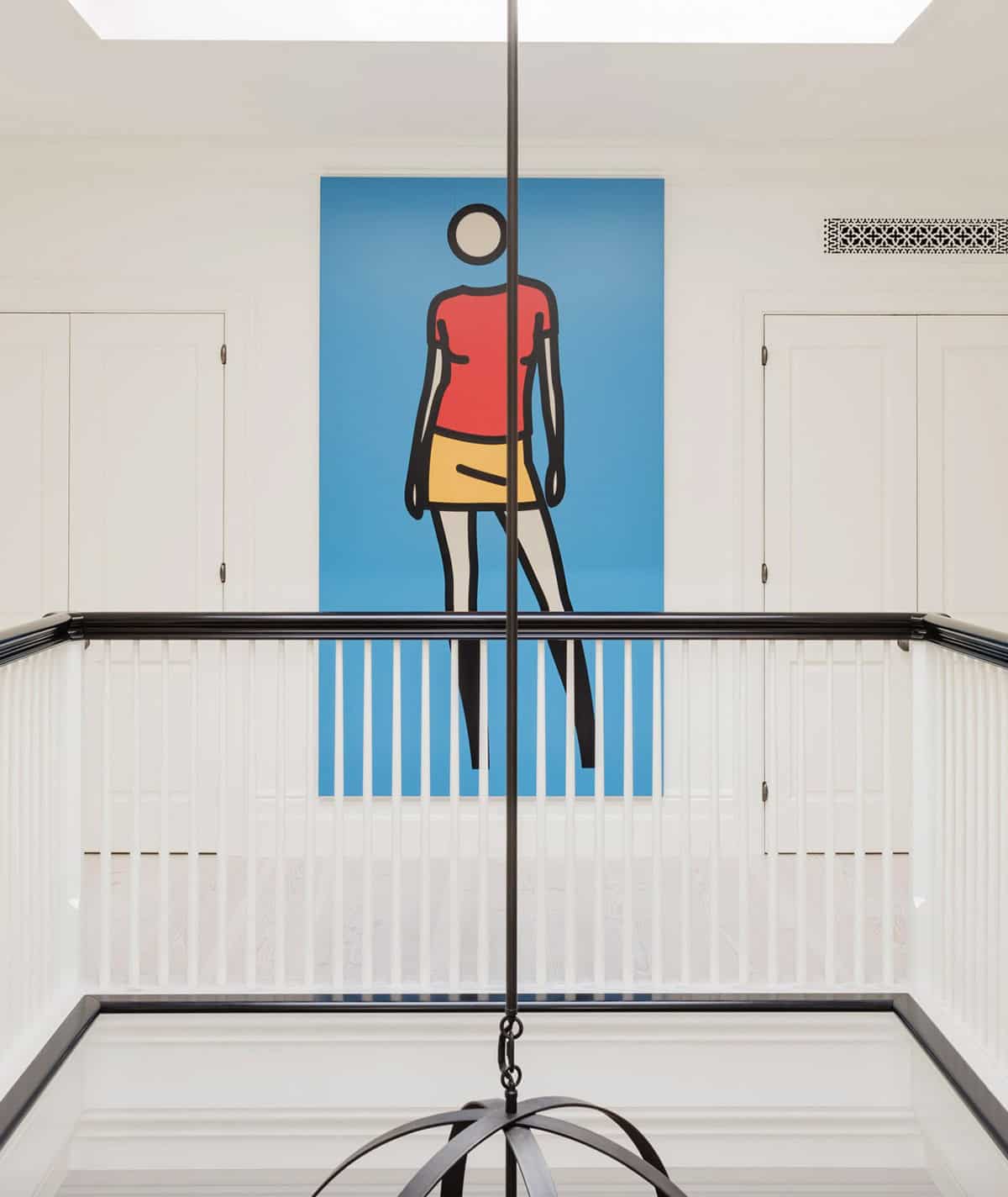 Staircase landing view of large Julian Opie-style figure painting on upper gallery wall