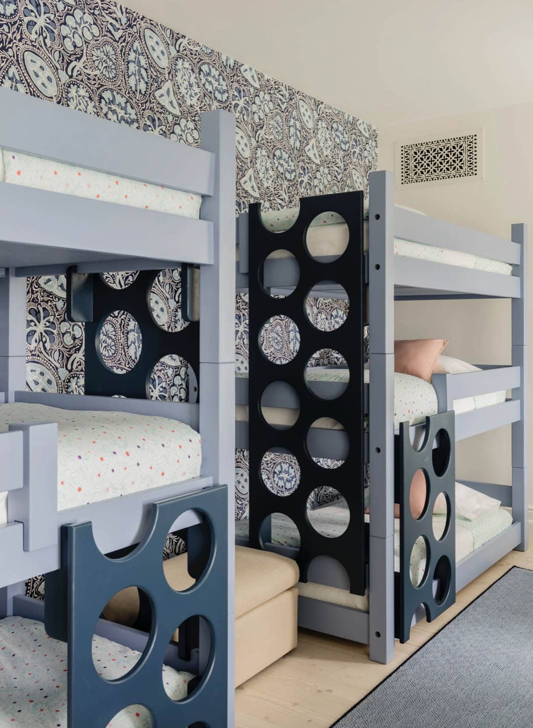 Kids' bunk room with four blue-painted bunk beds, circle-cutout ladders, and navy paisley wallpaper