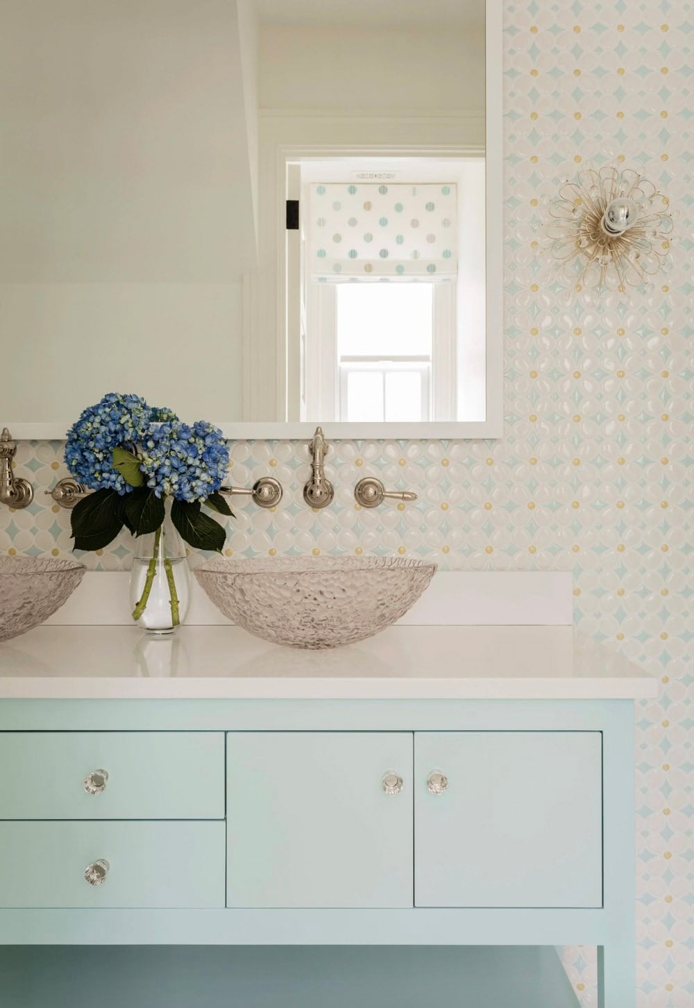 Children's bathroom with mint vanity, crystal vessel sinks, diamond-patterned tile wallpaper, and starburst sconce