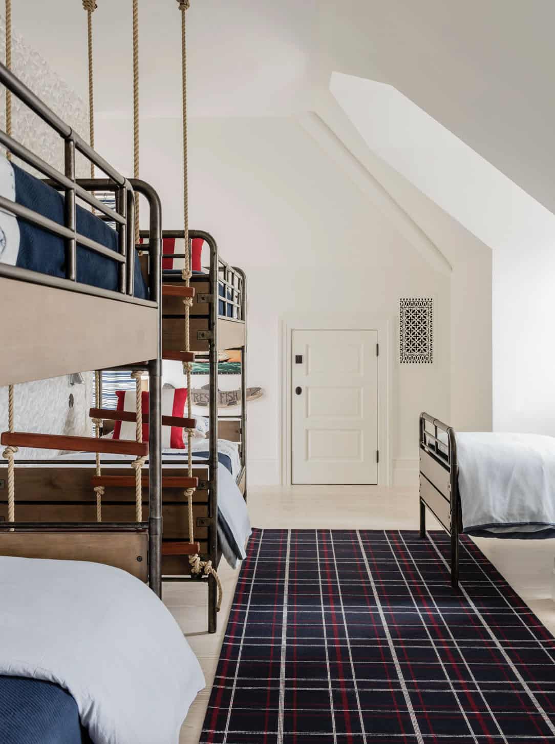 Attic bunk room with industrial pipe bunk beds, rope ladder, navy plaid rug, and sloped ceiling