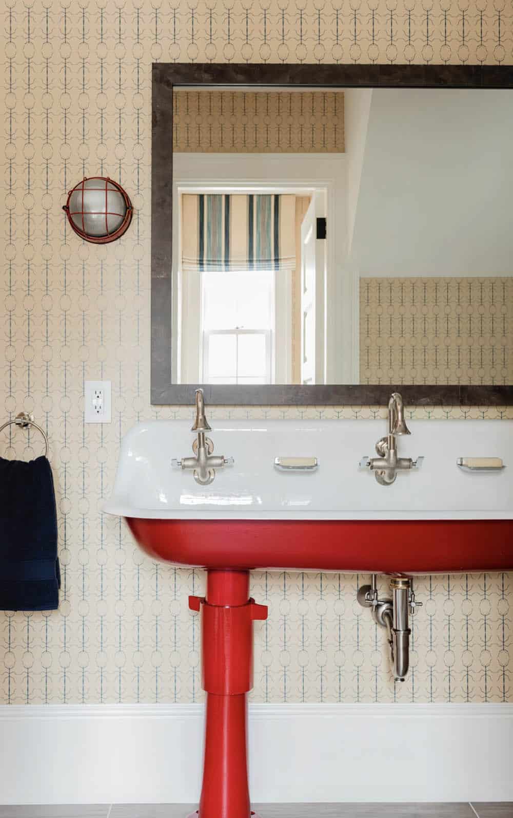 Kids' bathroom with red double trough sink, arrow-print wallpaper, industrial porthole sconce, and steel-framed mirror