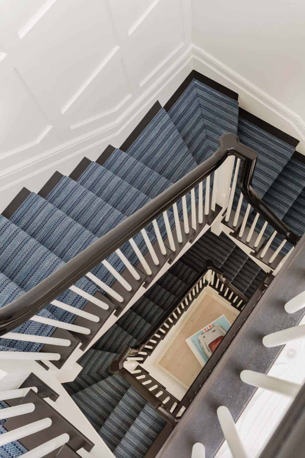 Aerial view down stairwell with blue striped carpet runner, black handrail, and white balusters