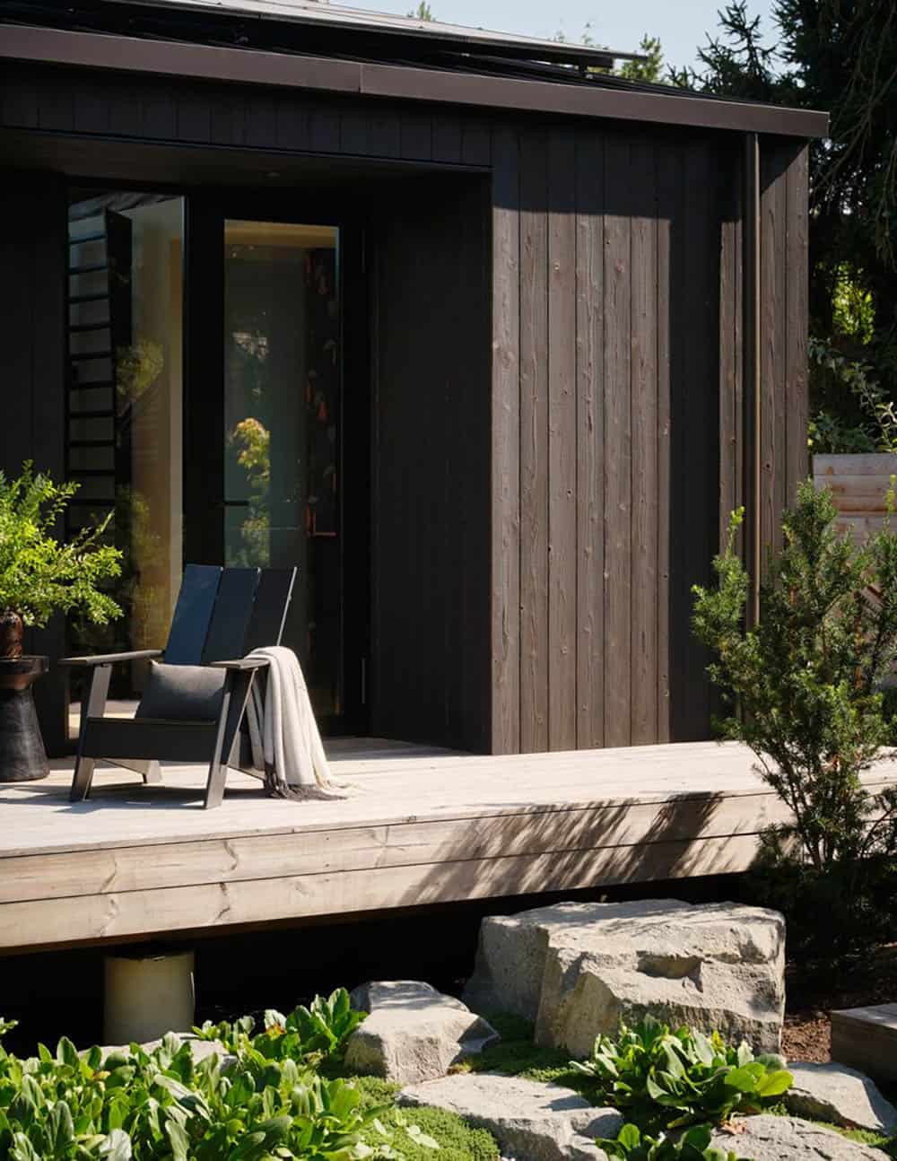 Dark vertical wood siding with sliding glass door opening to covered deck and chair
