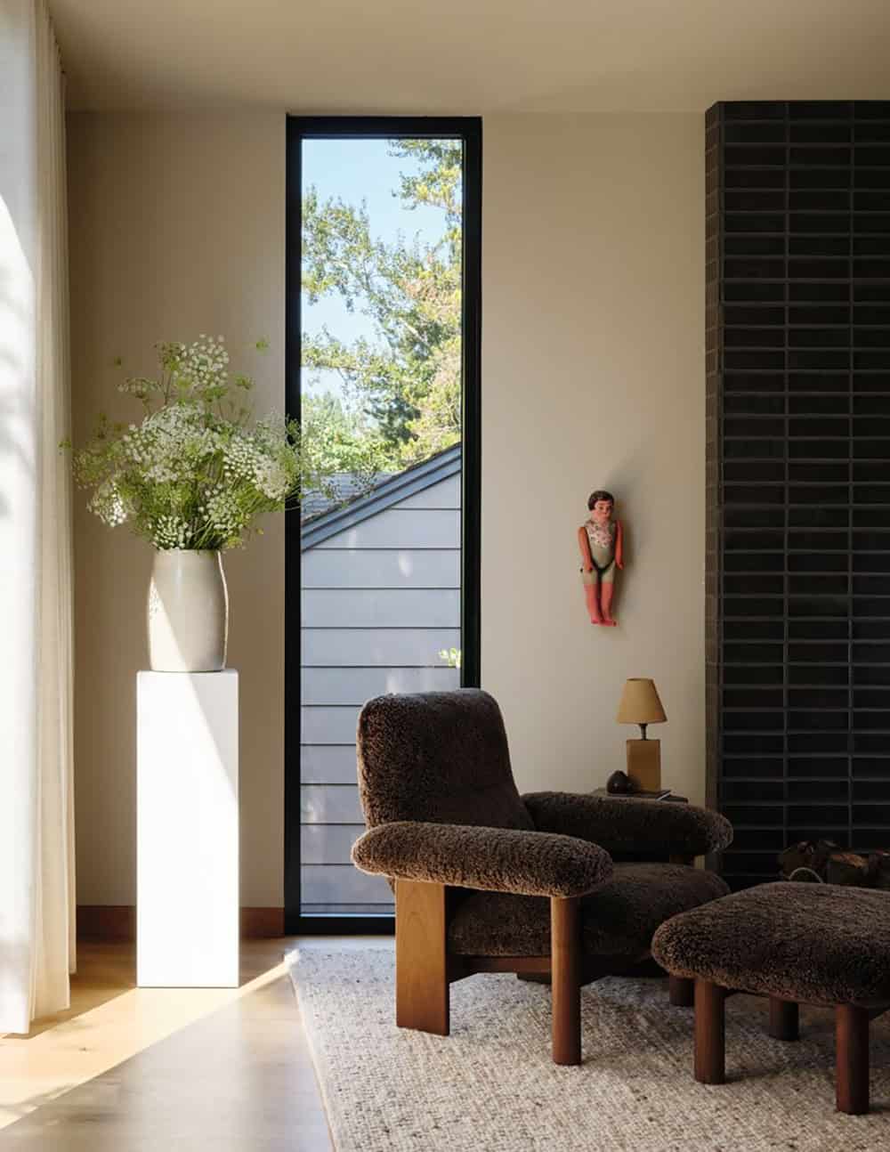 Tall narrow window with shearling lounge chair and dark brick fireplace surround